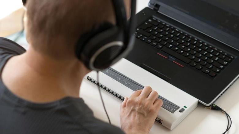 Person using a computer with Braille display 和 headphones